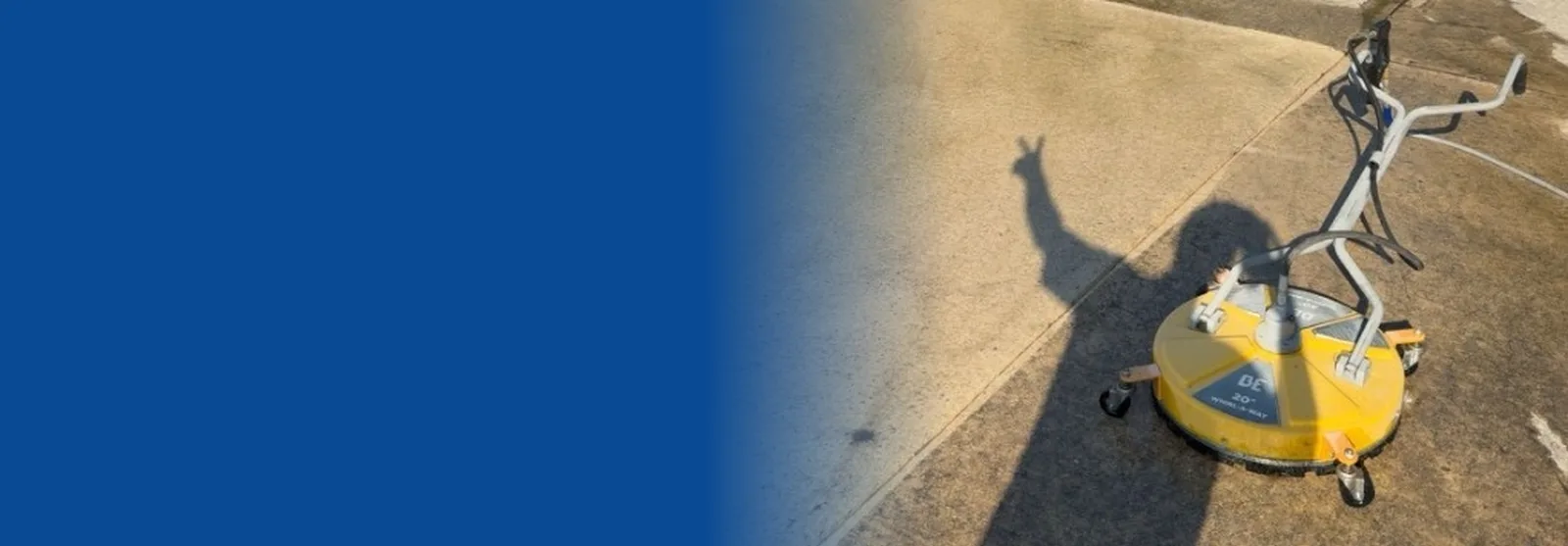 Surface cleaner machine on a half-cleaned concrete driveway with the operator's shadow flashing a peace sign